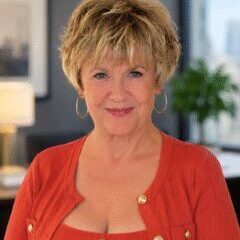 Mona Lee, owner of Mona Lee and Associates, smiling and wearing a coral sweater and gold earrings.